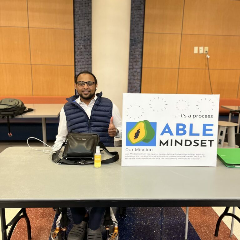 Addis Gonte of Able Mindset sitting at an event table with the Able Mindset logo signage.